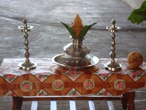 The kolam (designs made of rice flour paste) is first drawn. Within its boundaries, the traditional Tamil welcome is set up facing north, with the kuthuvillaku/lamps and the coconut with mango leaves placed in the kudam/pot